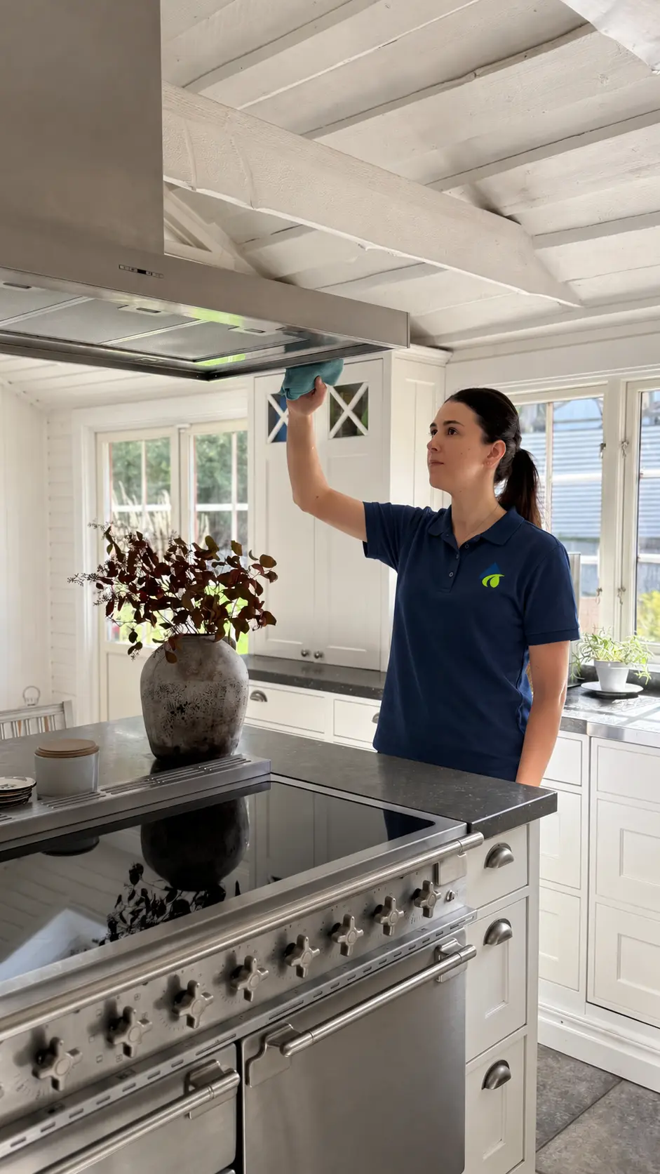 CleanHouse-personal rengör en köksfläkt i ett ljust kök
